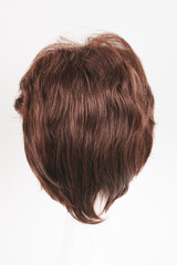 Naklejka premium Natural looking dark brunet wig on white mannequin head. Short brown hair on the plastic wig holder isolated on white background, back view.