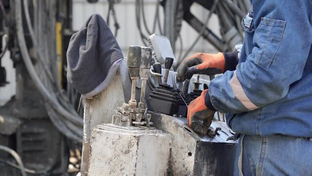 An unrecognizable builder is operating control levers on a drilling machine for efficient construction operations, close-up hands.