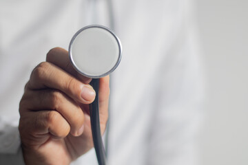 The doctor holds a medical stethoscope, embracing it against a white background.