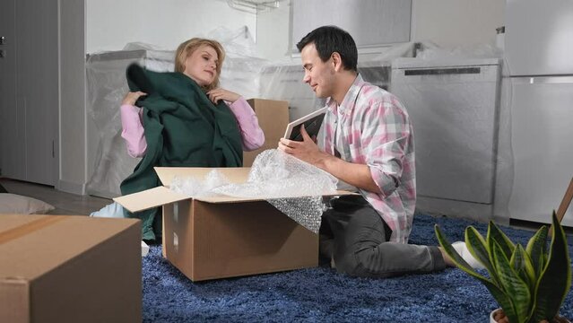 Couple move into new house. People pull things out box. Family unpack stuff. Home relocation. Real estate concept. Girl sit floor package item. Adult man buy flat. Team work unbox. Bubble wrap goods.