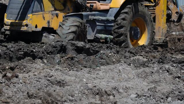 An excavator moves through the construction site, its wheels buried in mud, close-up.