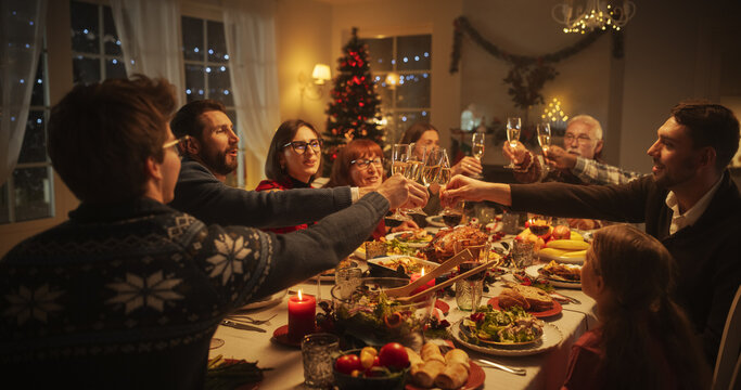 Christmas Dinner Together with Happy Parents, Children and Friends at Home. Close Up of Raising Champagne Glasses and Toasting, Celebrating a Holiday with a Delicious Turkey Meal in the Evening - Powered by Adobe