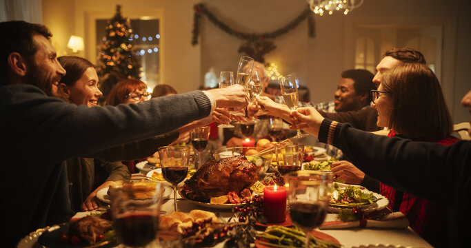 Christmas Dinner Together with Parents, Children and Friends at Home. Multicultural Family Raising Champagne Glasses and Toasting, Celebrating a Holiday with a Delicious Turkey Meal in the Evening