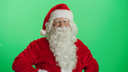 Studio Shot Isolated Mockup Template: Jolly Santa Claus Standing On Green Screen Chromakey Background With Hands Crossed, Looks At The Camera And Winks Cheerfully. Christmas, New Year, Celebration
