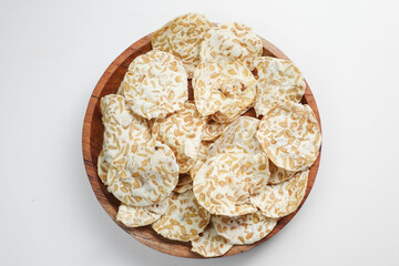 Keripik Tempe or Tempeh Chips are made from soybeans and served on a wooden plate. Isolated on white background.