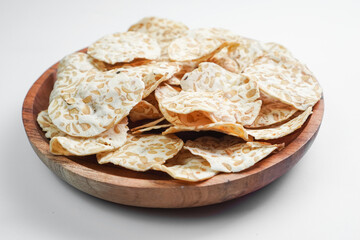 Keripik Tempe or Tempeh Chips are made from soybeans and served on a wooden plate. Isolated on white background.