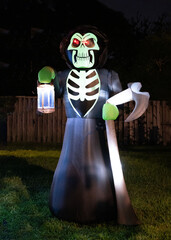 Halloween decoration of inflated skeleton with red eyes in a black robe with a glowing lantern and...