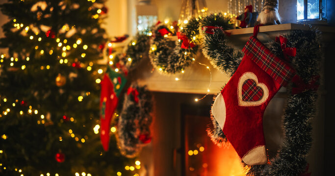 Empty Shot Depicting the Magic of Holidays on a Peaceful Snowy Christmas Eve: Close Up on Decorated Fireplace with Stockings Next to a Christmas Tree. Green and Red Garlands, Ribbons and Lights