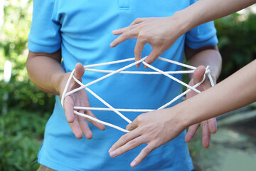 Close up two men playing with rope traditional game called cat cradle, use hands to hold  and...