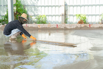 The construction technician is leveling the concrete floor with long trowel to be smooth.