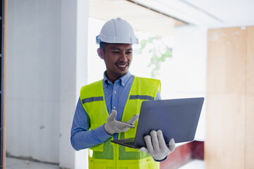 Asian construction worker using laptop at the construction site, industrial building design project concept. 