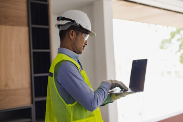 Asian construction worker using laptop at the construction site, industrial building design project concept. 