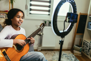 Young teenager playing guitar and recording vlog and music tutorial for the Internet.