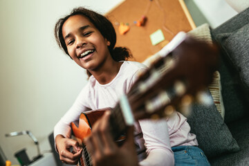African american teenage girl sitting on couch in her room and learning to play guitar - obrazy, fototapety, plakaty