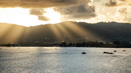 Stunning sunset with sun rays through clouds shining on mountain landscape and sea. Taken from Khao Khad Viewpoint in Phuket, Thailand.