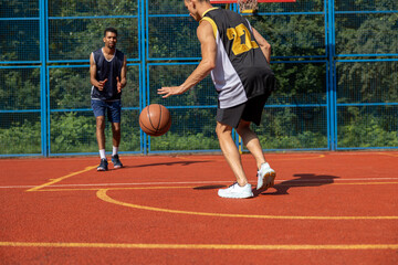 Two unrecognizable men playing basketball in court outdoors.