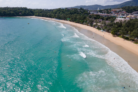 Aerial view of Kata Beach with surfers riding waves on surfboards during the low season. One of the popular travel destinations in Phuket, Thailand. Beautiful summer scenery of Andaman Sea
