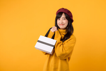Young Asian woman in her 30s, with a shopping paper bag, showcasing her style in a yellow sweater and red beret against a yellow background.