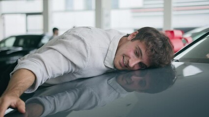Happy Caucasian man driver buyer excited guy client in auto automobile salon choose new auto stroking car hood hugging cuddling lying on vehicle buying transport enjoy purchase test drive rent service