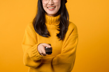 Cozy home scene featuring a young woman in her 20s, dressed in a yellow sweater, watching television with a remote control.