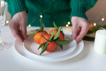 Woman is holding fresh organic tangerines with green leaves on the plate  in her hands. Christmas or New Year seasonal festive food concept