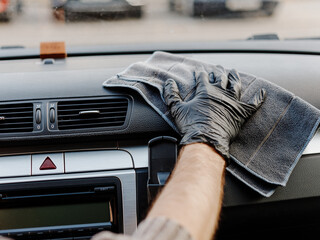 Man's hand in black glove cleaning car interior, dashboard and leather seats with microfiber cloth. Hand wipe down suede leather seat saloon interior.