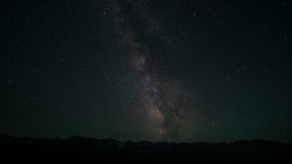 The Milky Way with a falling meteorite on the background of mountains. A bright colored stripe is a...