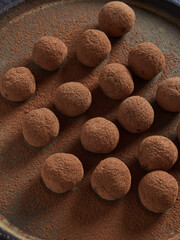 Healthy homemade raw treat, sugar free truffles made of dates, cocoa and nuts. Raw chocolate bliss balls dusted with cacao on a dark plate. Energy balls.