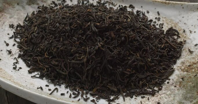 Top view of unpressed pu-erh tea forming a heap on a rectangular ceramic plate. Rustic wooden table. Table spin. 
