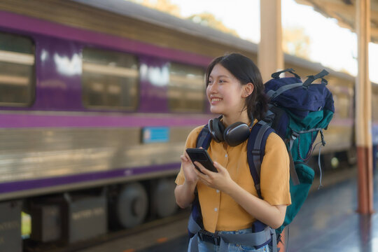 Young Asian woman traveler with a backpack on the railway, Backpack at the train station with a traveler, Travel concept. Woman traveler tourist walking at a train station.