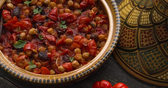 Moroccan vegan tagine made of Ethiopian eggplant and chickpea in an open traditional tagine pot. A few Ethiopian eggplants next to it. Top view, table spin.