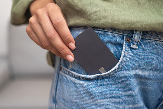 Streamlined shopping: A lady's hand pulls a dark credit card with a chip from her jeans pocket, simplifying online payments for ordered goods, the epitome of convenient shopping. 