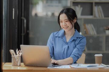 Fototapeta premium Asian businesswoman working on laptop sitting at desk in office, 
