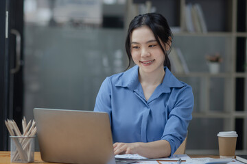 Asian businesswoman working on laptop sitting at desk in office, 