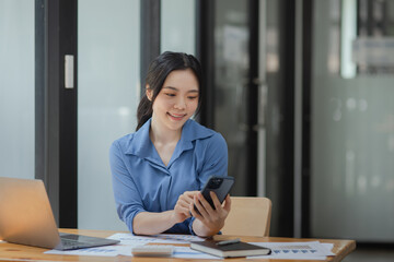 Asian businesswoman using smartphone sitting at desk in office, working online, 
