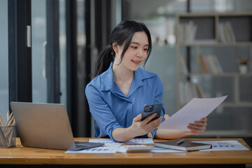 Asian businesswoman using smartphone sitting at desk in office, working online, 