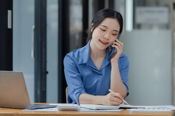 Asian businesswoman using smartphone sitting at desk in office, working online, 