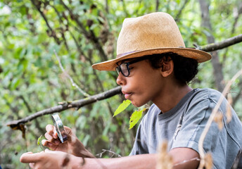 Boy looking at a leaf with a magnifying glass looking for the microworld of nature - Concept of...