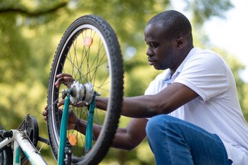 Dark-skinned man fixing s problem with a bike and looking involved