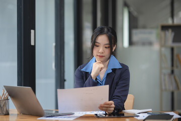 Asian woman working with document papers and laptop sitting at desk workplace office.