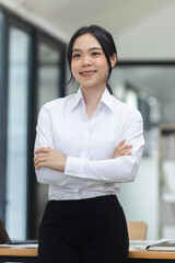 Asian woman arms crossed and standing at office desk.