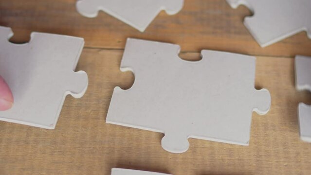 Close up view of businessman hands trying to connect assembling jigsaw puzzle and join pieces on conference table in office, team help and support, finding right solutions in teamwork concept