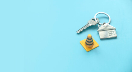Concept of under construction or fixing for home, property or real estate.House key with traffic cone over a blue background with copy space.