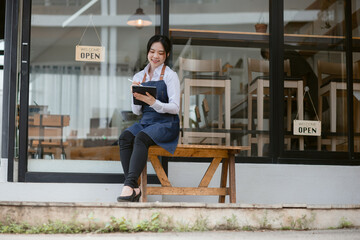 Fototapeta premium Happy smelling Asian woman owner with open sign broad and ready to service, Small startup business concept.