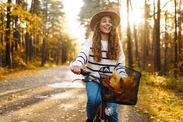 Young woman in a stylish sweater and hat rides a bicycle, feels freedom, enjoys the autumn weather...