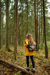 Woman traveler in a bright coat walks along a wooden path among the wetlands. A tourist with a backpack walks through the forest. Travel, nature concept.