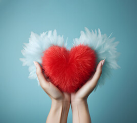 Fluffy red heart with feather wings in female hands, creative romantic love concept.