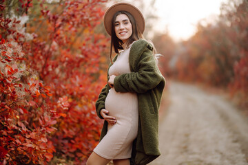 Stylish pregnant woman walks in an autumn park, happily expecting a baby. Happy pregnancy....