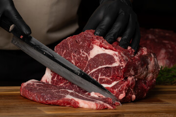 The butcher wearing black gloves cuts the meat with knife on wooden cutting board.Close-up piece of...