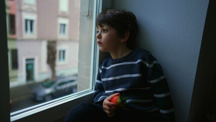 Bored sad emotion of little boy sitting by window staring at view in melancholy, child wanting to...